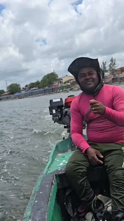 Ostricultor sentado na popa de um pequeno barco a motor no estuário, a caminho do viveiro.