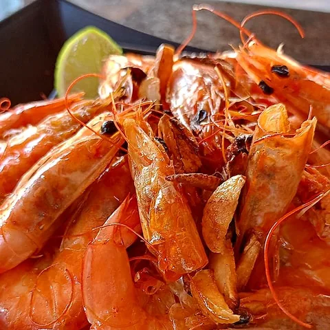 Camarões inteiros e dourados, salpicados de alho frito, com gomos de limão.